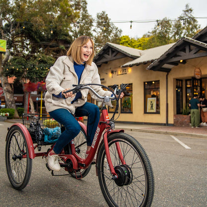 Woman riding a red electric bike on a street with buildings and trees in the background