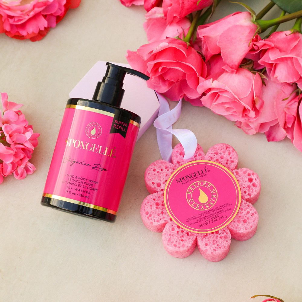 Pink body lotion bottle and flower-shaped sponge with pink flowers in the background