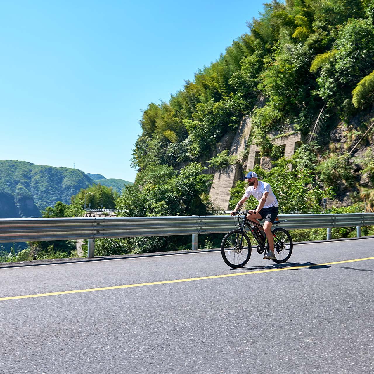 Person cycling on a road with greenery and mountains in the background
