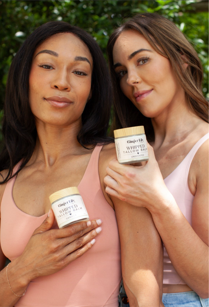 Two women holding jars of whipped body butter against a green outdoor background