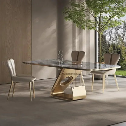 Modern dining table with marble top and gold base in a room with large windows.
