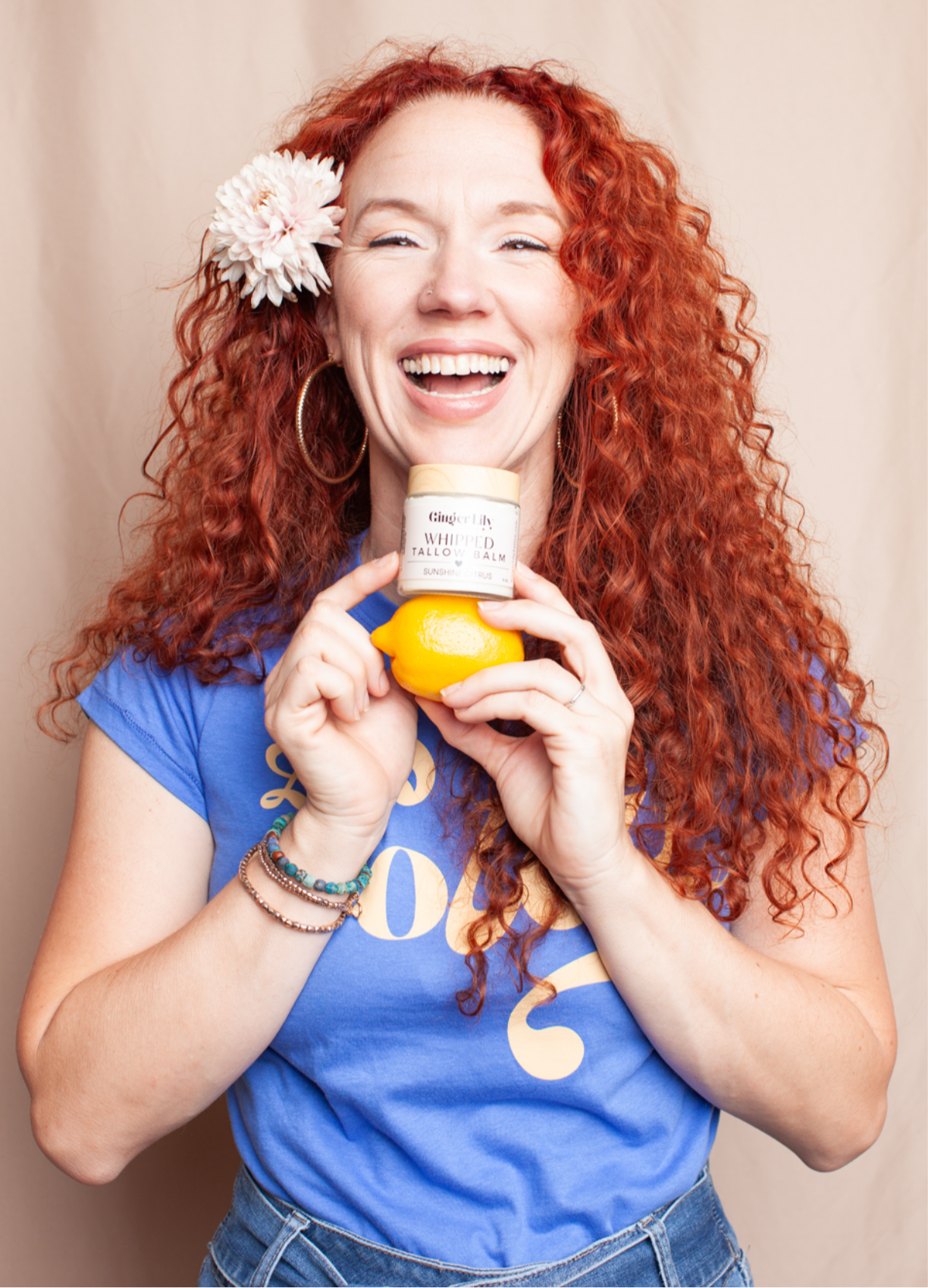 Woman with red hair holding a bottle of Ginger Lily Tallow against a beige background