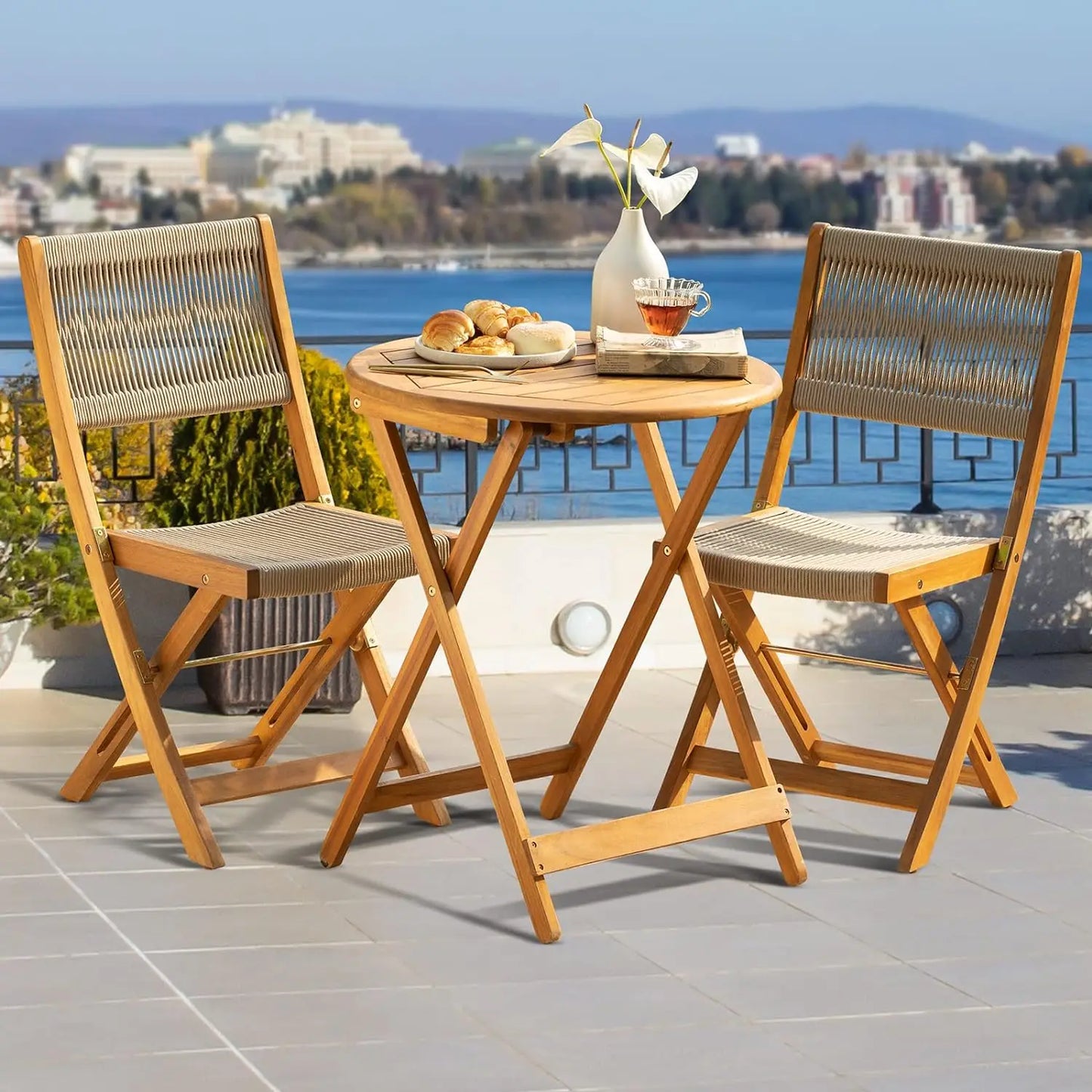 Wooden outdoor table with two chairs on a patio with a scenic view of water and buildings.