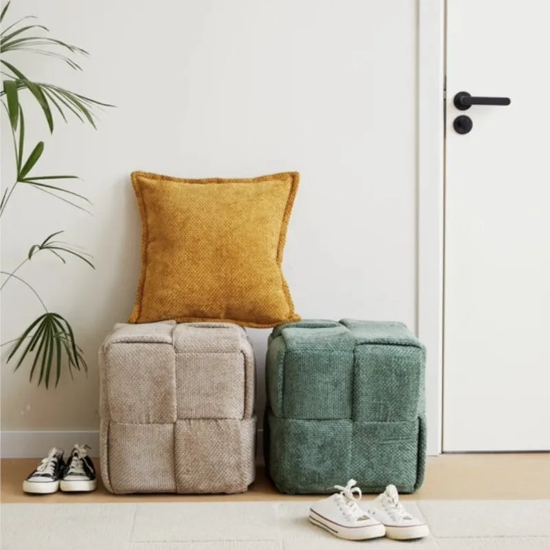 Two Sugar Stool ottomans with a yellow pillow and white sneakers in a room.