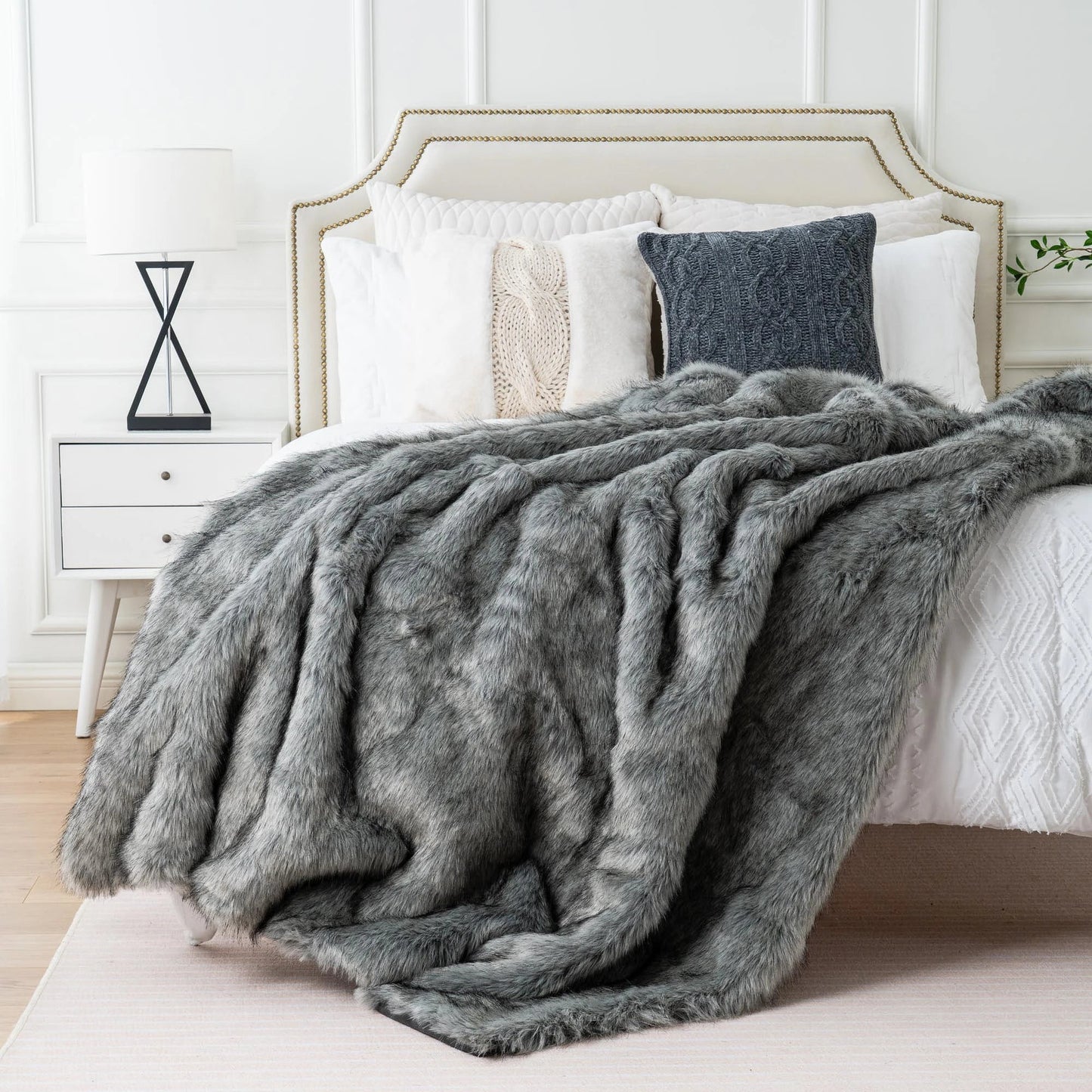Gray fur throw blanket draped over a bed with white bedding and pillows.