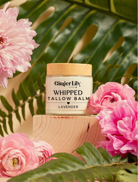 Ginger Lily whipped tallow balm jar with pink flowers and green leaves in the background