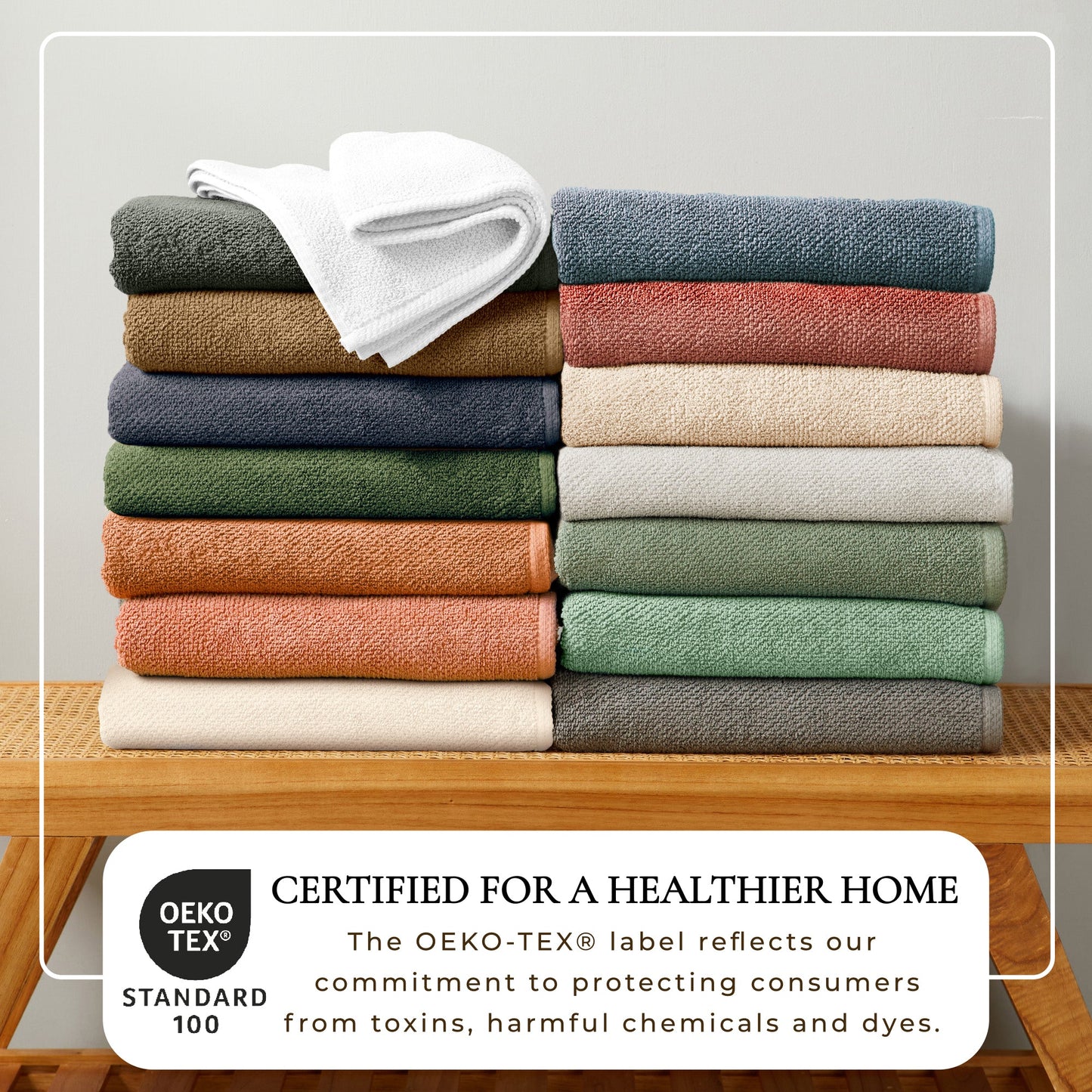 Stack of folded towels in various colors on a wooden table with OEKO-TEX certification label.