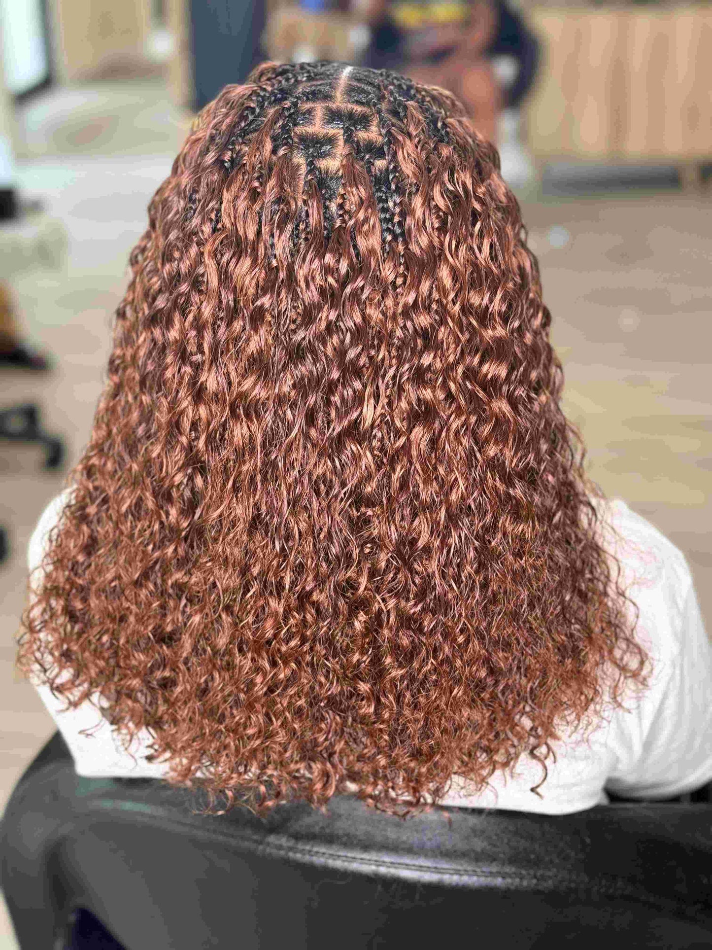 Person with curly hair styled in cornrows, sitting in a chair.
