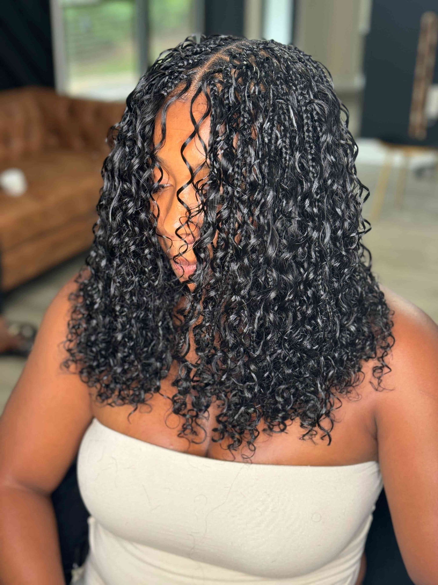 Person with curly hair in a room with a couch and chair.