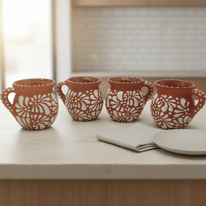 Four terracotta mugs with floral patterns on a light wooden surface.