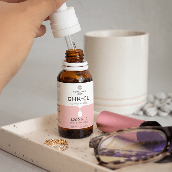 Bottle of GHK-CU serum with dropper on a tray with a cup and glasses in the background