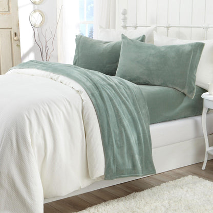 Green blanket and pillows on a white bed in a bedroom setting