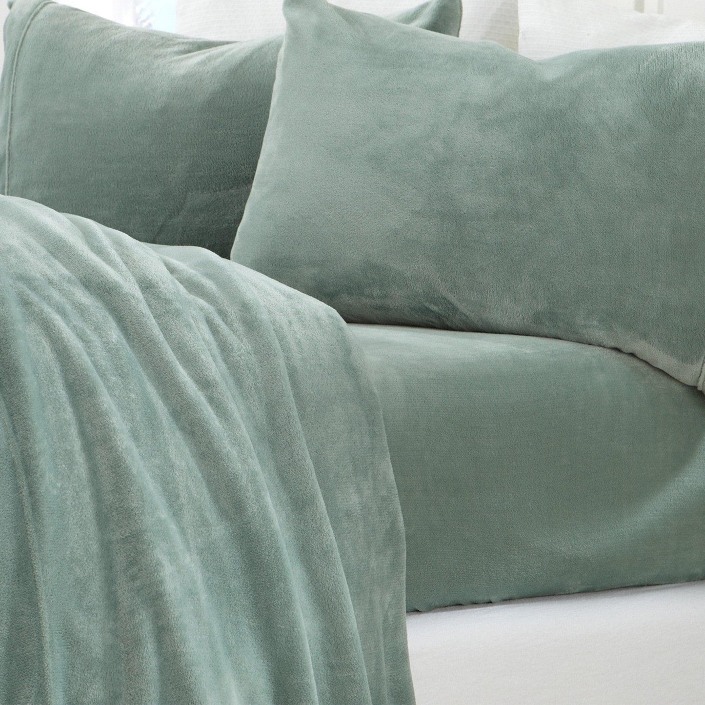 Green velvet pillows and blanket on a white surface