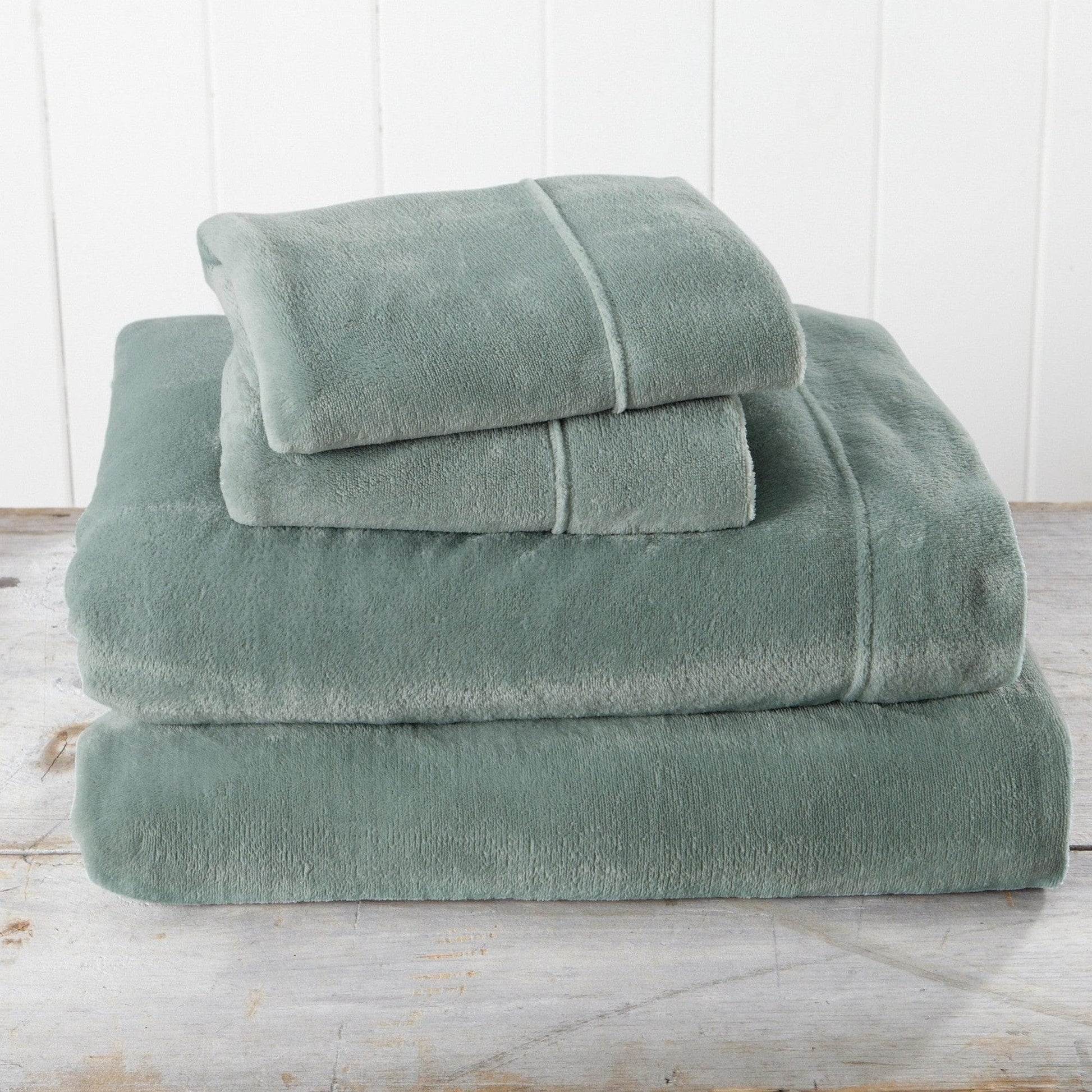 Set of green towels stacked on a wooden surface with a white wooden panel background