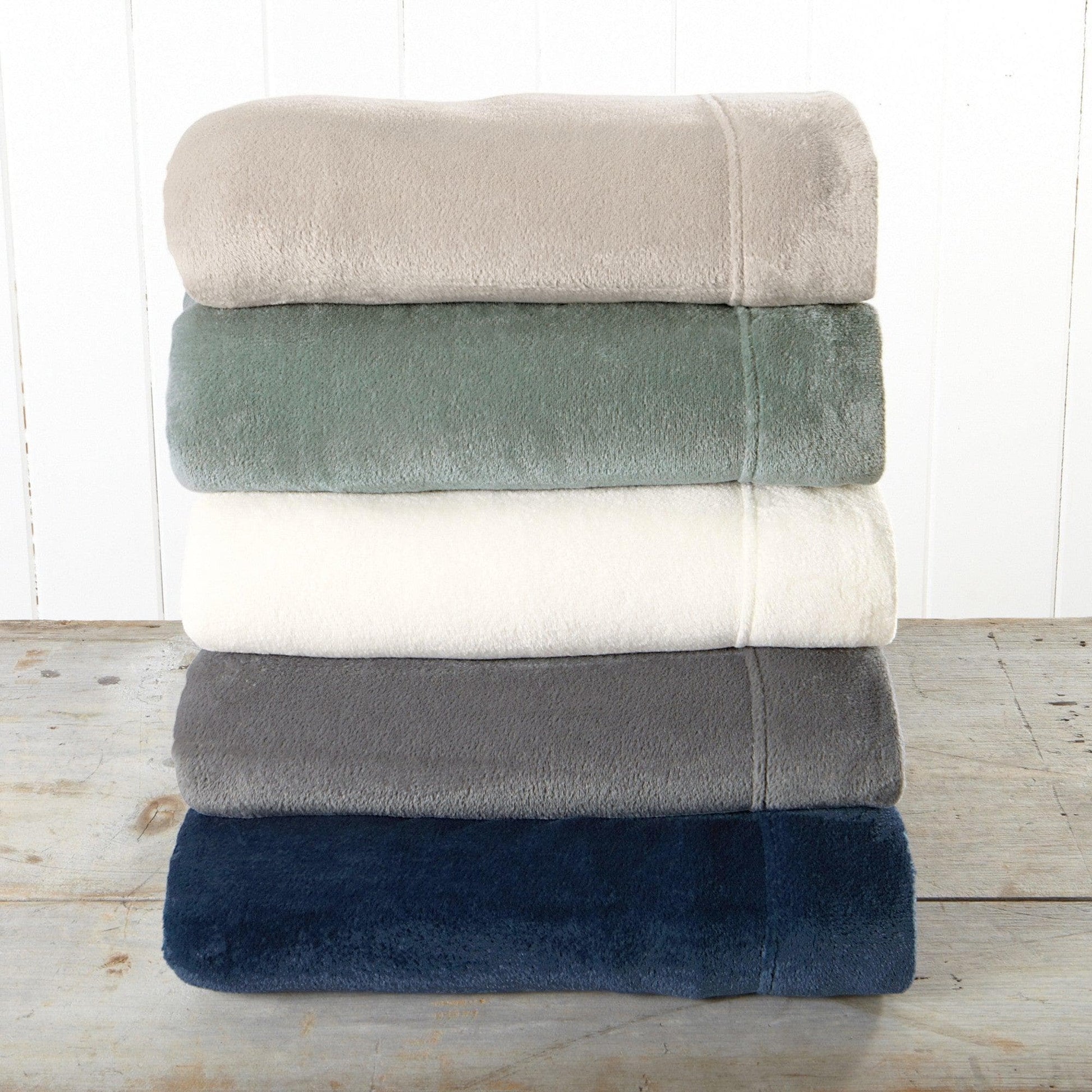 Stack of folded towels in beige, green, white, gray, and blue on a wooden surface with a white background.