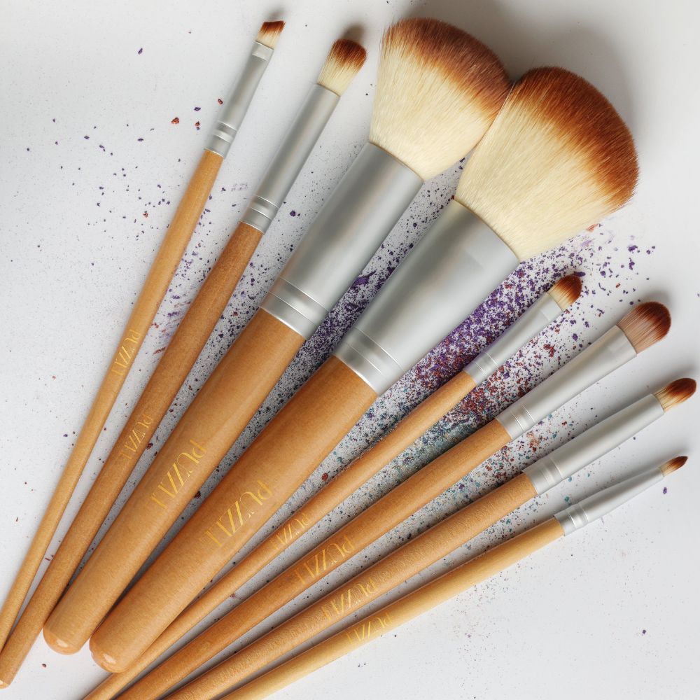 Set of makeup brushes with wooden handles and metallic ferrules on a textured white background.