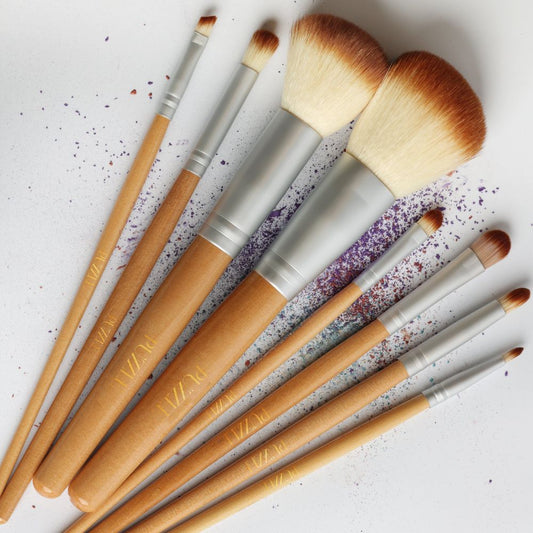 Set of makeup brushes with wooden handles and metallic ferrules on a textured white background.