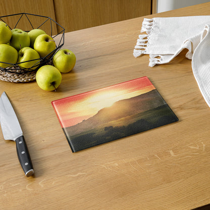 Glass cutting board with mountain design on a wooden table with apples and a knife.