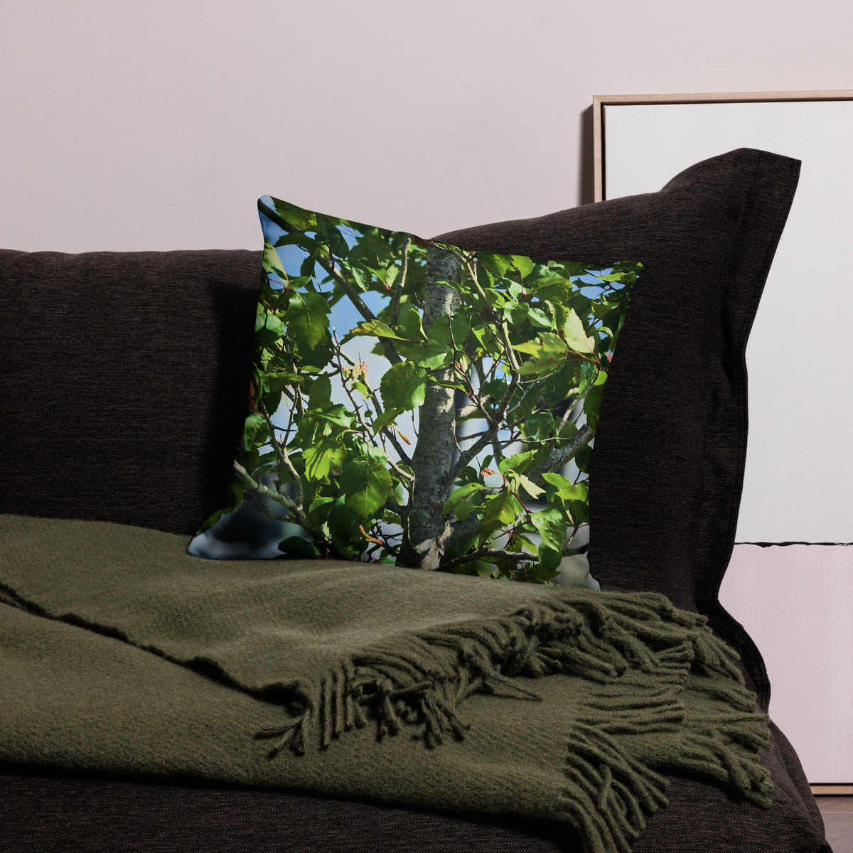 Decorative pillow with a nature print on a dark sofa with a green blanket.