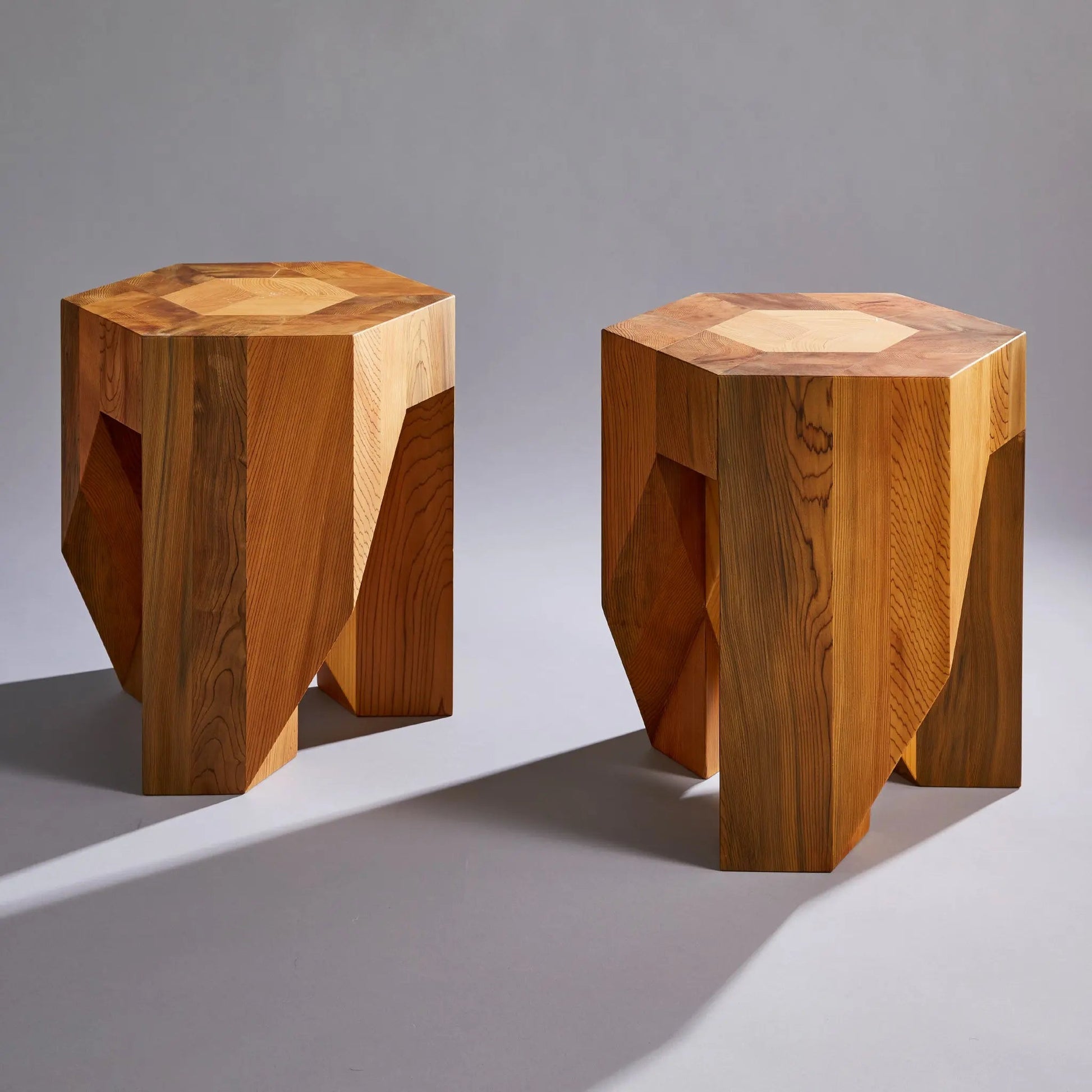 Two hexagonal wooden stools on a gray background